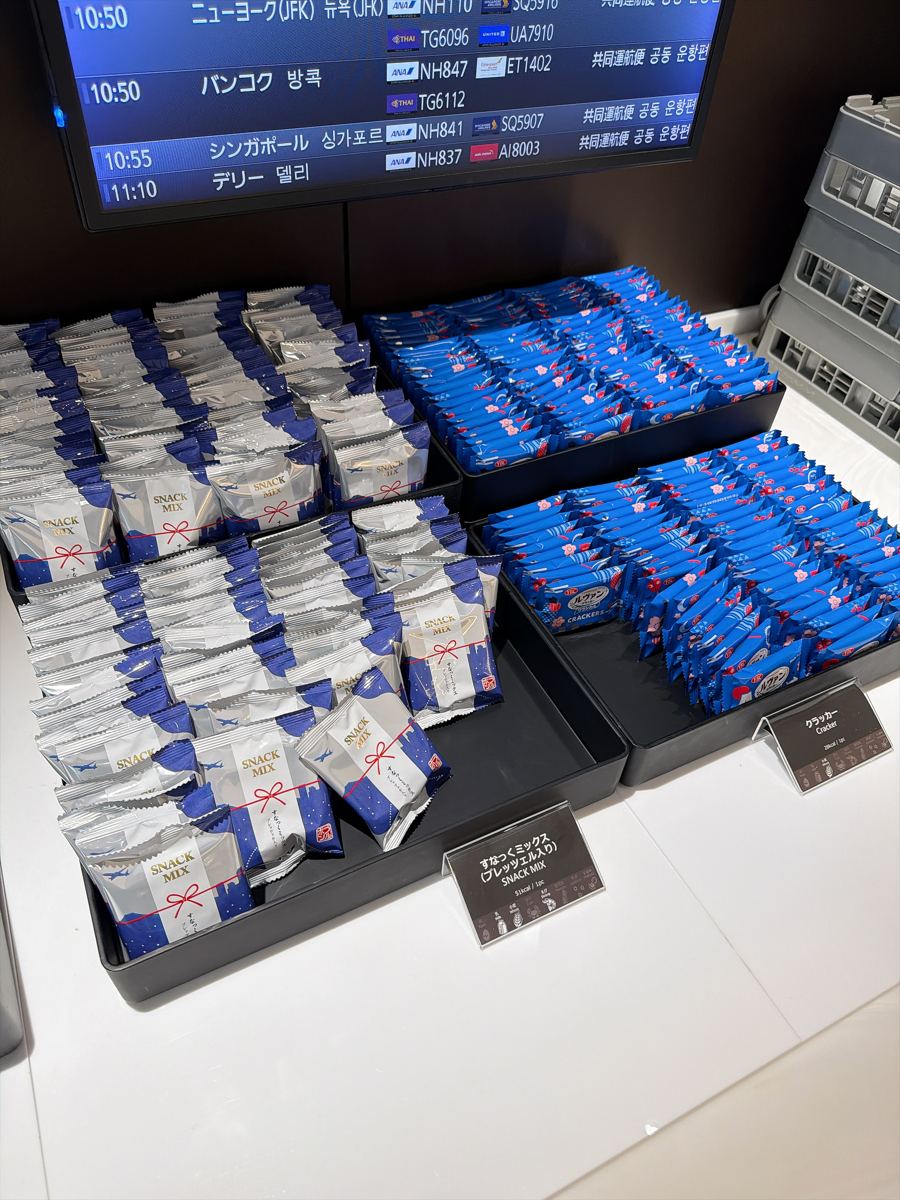 ANAラウンジのスナックミックスとクラッカー。奥に出発案内の画面